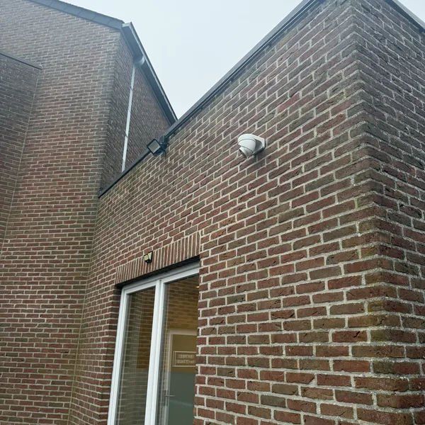 Projecteur LED blanc et caméra de surveillance installés en hauteur sur la façade en brique du Centre Paramédical de Wanfercée-Baulet